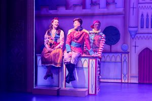 Snow White and the prince are sitting on a low wall singing romantically. Muddles is standing behind the wall making a face. Louisa is out of sight bracing the wall.