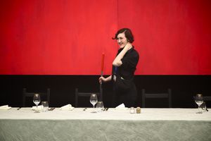 Louisa with a broom behind a table.