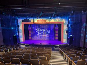 A view from the back of the theatre looking towards the stage where a Sleeping Beauty banner is projected onto a cloth.
